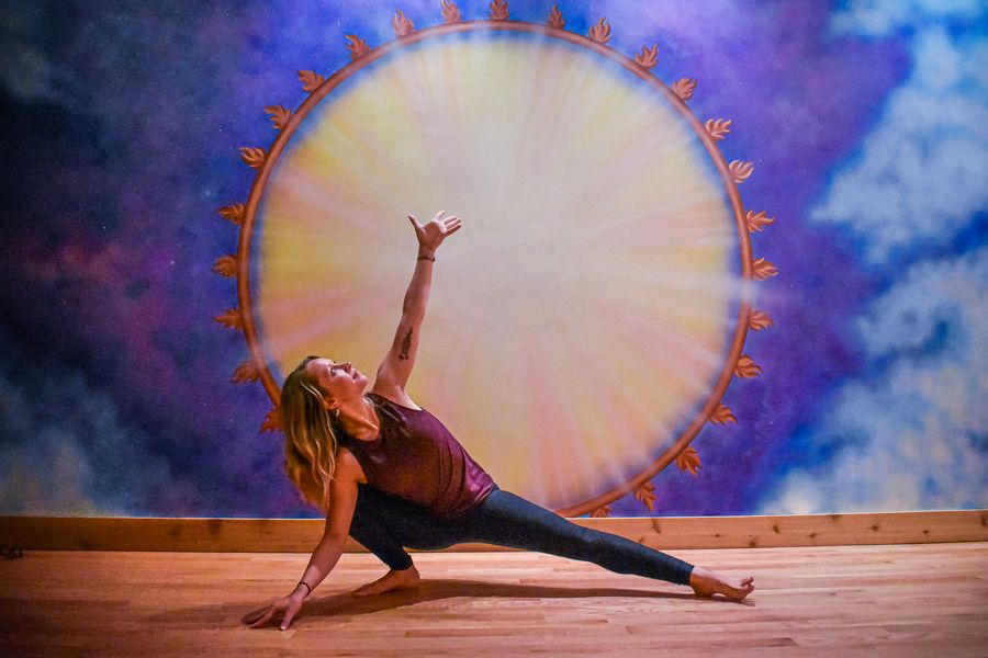 A side plank variation with one arm reaching up, in front of the sun mural