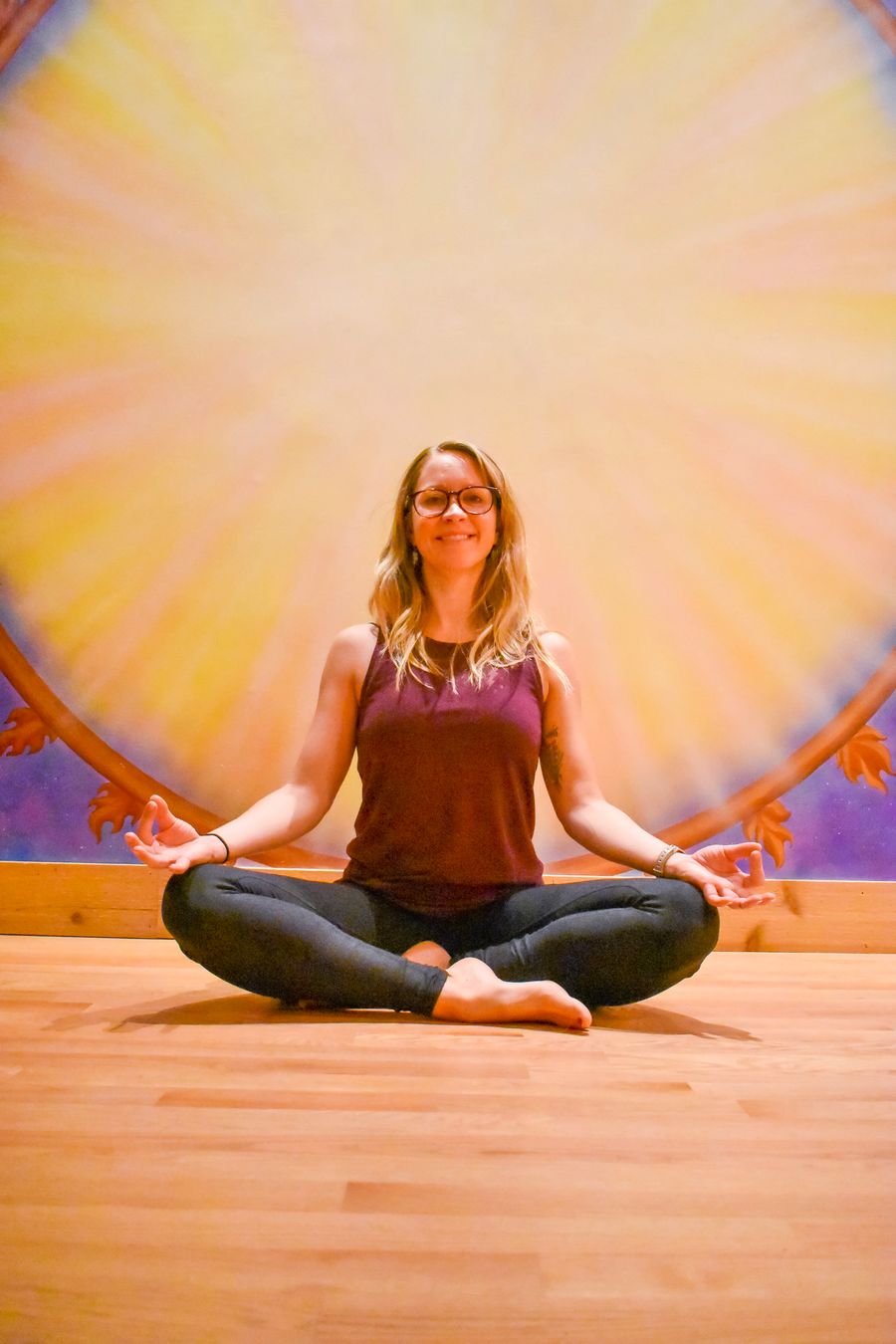 Seated in meditation and smiling, in front of the sun mural
