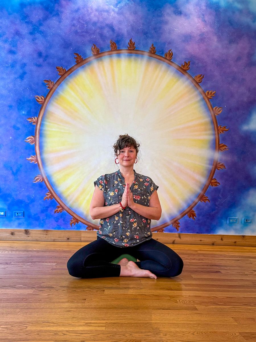 Seated cross-legged with the palms together, centered in the sun mural