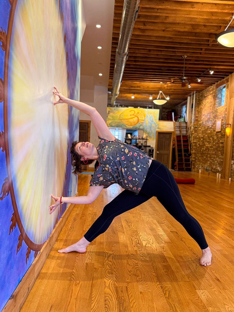 A triangle pose reaching along the mural wall, the long studio behind
