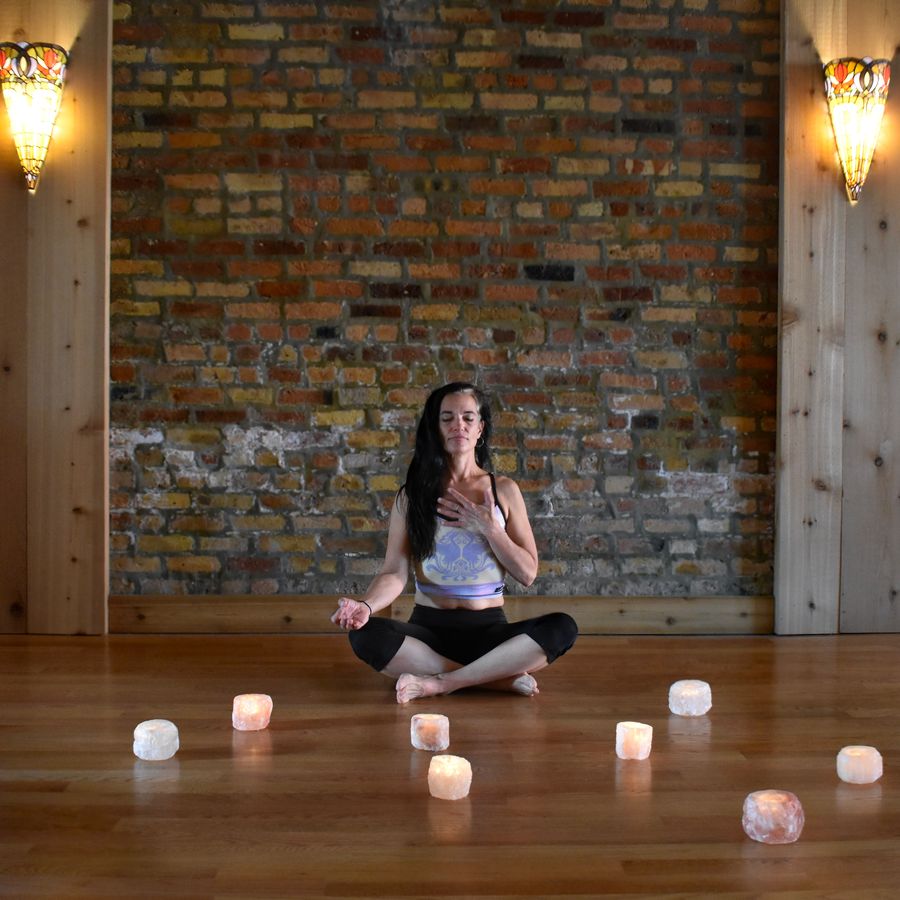 Seated cross-legged, ringed by glowing salt lamps by the brick wall