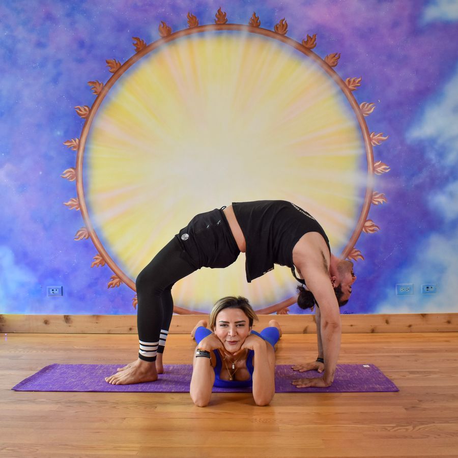 A partner pose at the sun mural: one person arches over the other in a backbend