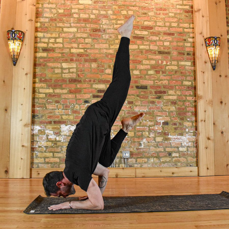 A forearm balance with one leg raised high, against the brick wall