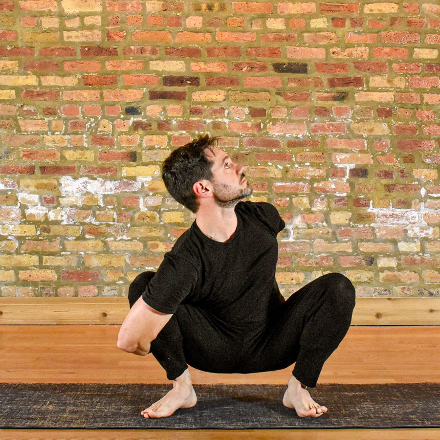 A deep squat with the arms wrapped forward, against the brick wall
