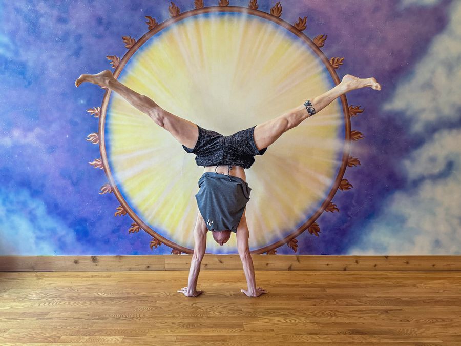 A handstand with legs split wide in front of the painted sun mural