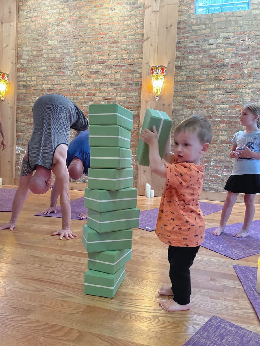 A toddler building a tower of yoga blocks while the grown-ups hold downward dog