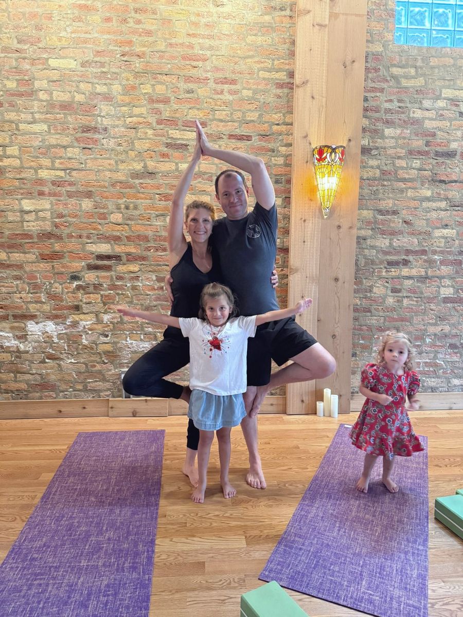 A mom and dad in partner tree pose with their daughters in front of the brick wall
