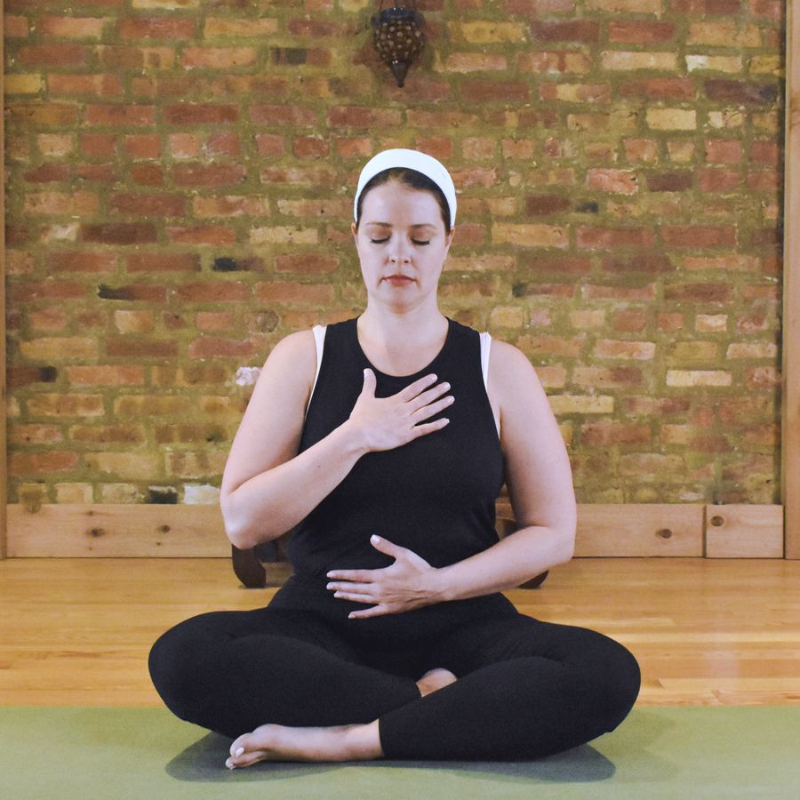 A student sitting cross-legged with one hand on the chest and one on the belly