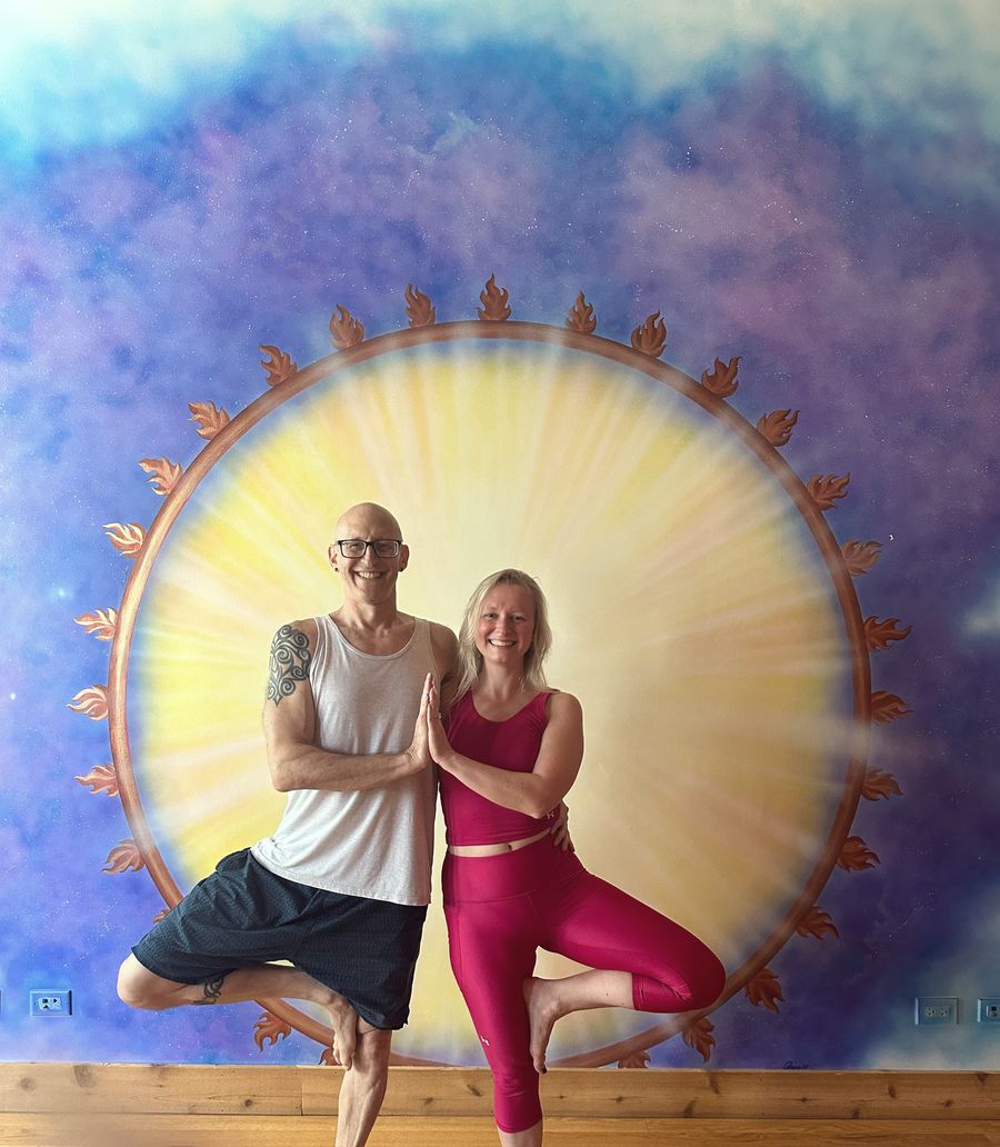 Rich and Nora, the founders, in tree pose in front of the painted sun mural at Chi Yoga Shack