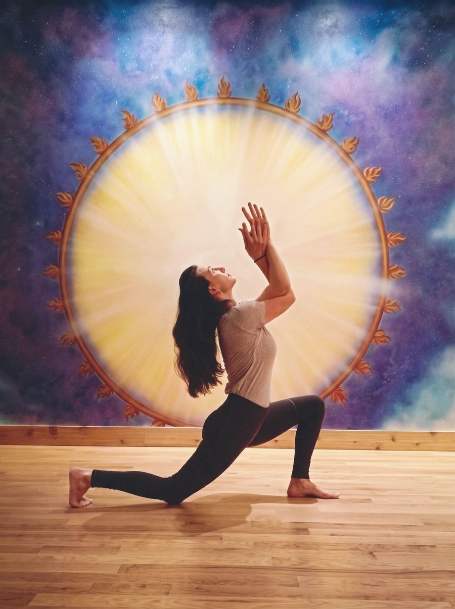 Nora Gonshak in a low lunge with her hands raised, in front of the painted sun mural