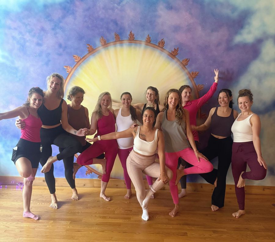 A group of friends laughing in tree pose in front of the painted sun