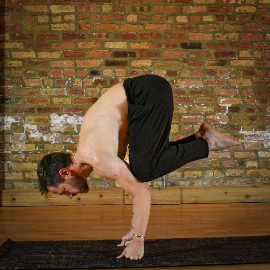 An arm balance with the knees tucked onto the arms, in front of the old brick wall