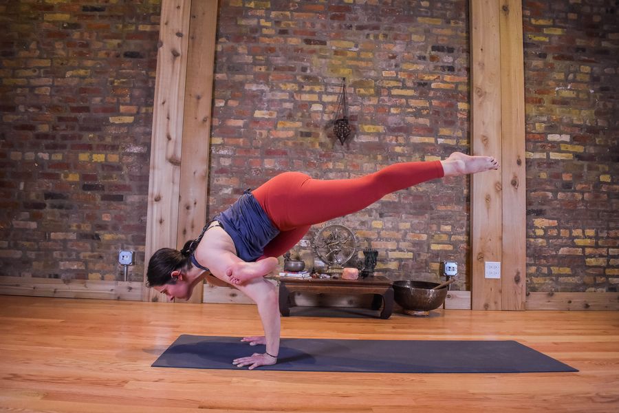 An arm balance with one leg stretched long behind, beside the brick wall