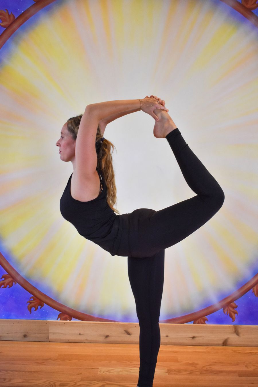 A dancer's pose, one foot held high overhead, against the painted sun mural