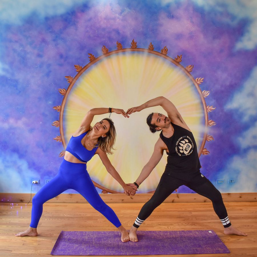 Two people in side bends, their arms joined overhead in the shape of a heart, at the sun mural